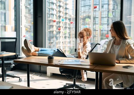 Joyful women chatting while working on laptop in coworking space Stock Photo