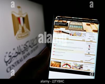 Person holding smartphone with webpage of monetary authority Central Bank of Egypt (CBE) on screen with logo. Focus on center of phone display. Stock Photo