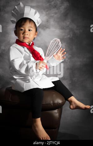 A toddler girl portrait is holding a whisk while sitting on a chair. Stock Photo