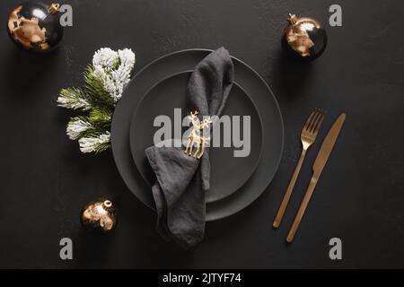 Christmas table setting with black plate and golden decorations on black background. Stock Photo