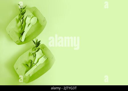 Eco disposable paper tableware and wooden cutlery on green background. Stock Photo