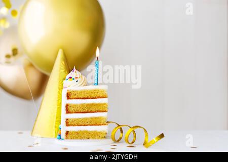 Slice of birthday cake with single blue birthday candle and gold birthday balloons Stock Photo