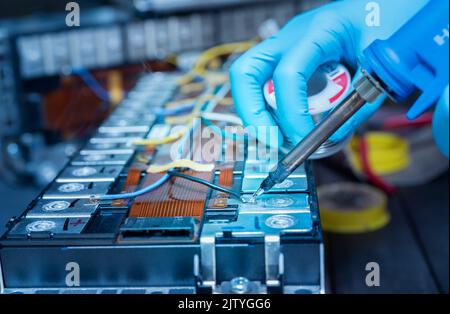 Technician use soldering iron to solder metal and wire of lithium-ion rechargeable battery. Repair module of Li-ion battery. Engineer hand holds solde Stock Photo