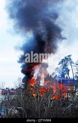 Strong fire. The house is on fire behind the trees. Strong fire and black column of smoke. Image is out of focus Stock Photo