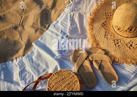 Top view of beach accessories. Straw hat, bag, flip flops on sand at beach. Stock Photo