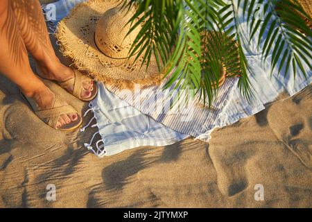 Top view of beach accessories. Straw hat, bag, flip flops on sand at beach. Stock Photo