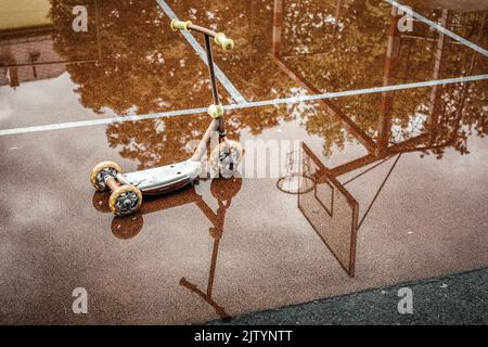 Reflection of children's scooter in the puddle at playground. Rainy weather. Stock Photo