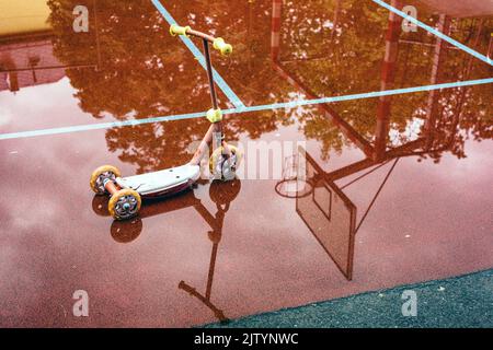 Reflection of children's scooter and basketball hoop in the puddle at playground. rainy weather Stock Photo