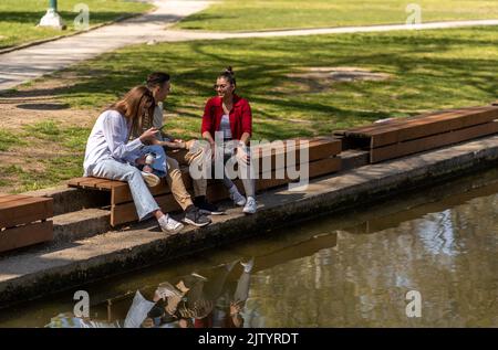 Resting with friends. Three groupmates standing together with other students on the path, relaxing after classes outside the university. Stock Photo