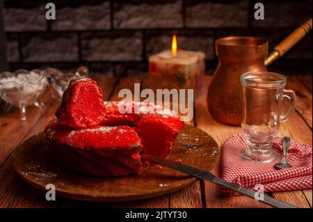A knife cut red decorated donut on wooden table and empty glass cup and coffee pot on table Stock Photo
