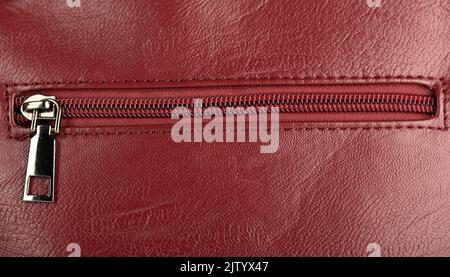 Closed zip fastening on burgundy leather surface. Copy space. Stock Photo