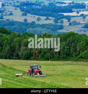 Red Massey Ferguson 7719 S tractor & Claas Disco 3200c swathing hay - hillside farmland pasture, scenic Wharfedale countryside, Yorkshire, England UK. Stock Photo