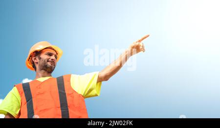 A portrait of a worker stands with confidence in an orange work suit and safety helmet against the sky. Smart industrial worker work concept. Stock Photo