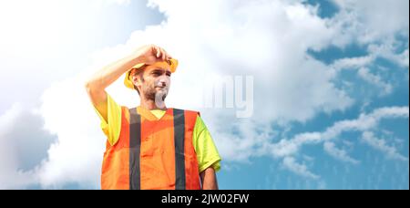 A portrait of a worker stands with confidence in an orange work suit and safety helmet against the sky. Smart industrial worker work concept. Stock Photo