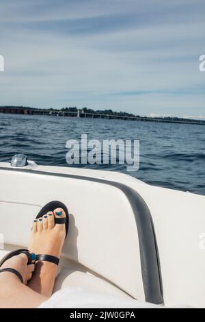 feet with blue toenails and black toe sandals resting on bow of boat in Lake Stock Photo