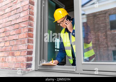 builder with clipboard and calling on smartphone Stock Photo