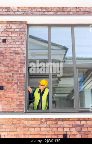 male builder in helmet looking out window Stock Photo