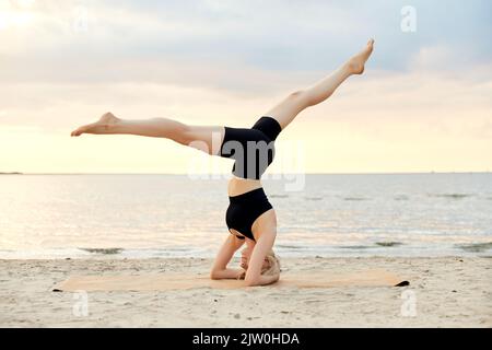 woman doing yoga headstand on beach Stock Photo
