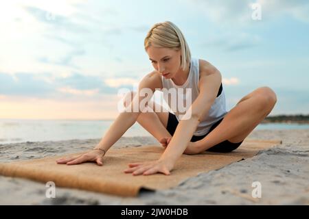woman doing yoga stretching pose on beach Stock Photo