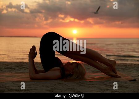 woman doing yoga plow pose on beach Stock Photo