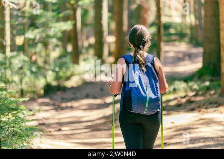 Woman walks through the forest. View from the back, close-up. Carries a backpack and hiking poles. Forest hiking path Stock Photo