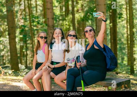 Mountaineers take selfie with phone on a wooden bench. Forest in background Stock Photo
