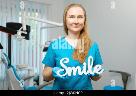 Happy caucasian female dentist with smile sign in dental office posing and looking at camera Stock Photo