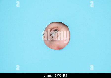 Woman peeking out of hole in blue paper background.  Stock Photo