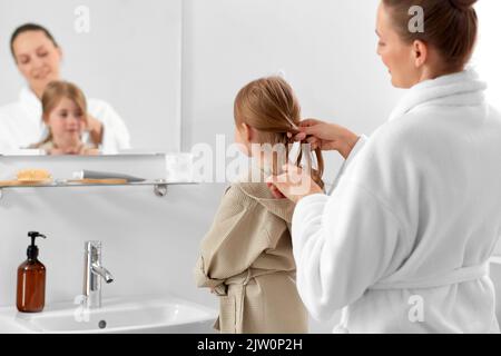 mother and daughter braiding hair in bathroom Stock Photo