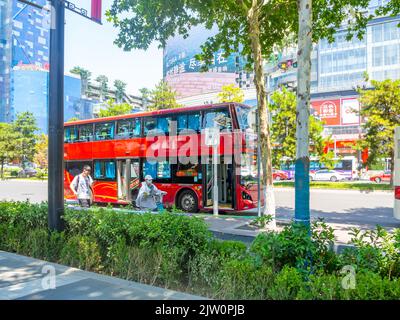 A tourist double-decker bus is waiting for passengers in the downtown district. Chinese people are walking in the scene. Stock Photo