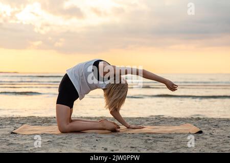 woman doing yoga camel pose on beach Stock Photo