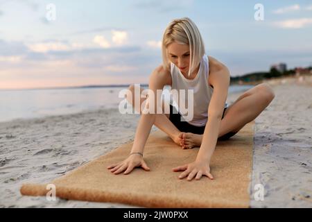 woman doing yoga stretching pose on beach Stock Photo