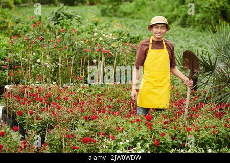 Smiling garden worker standing among blooming flower with spade in hand Stock Photo