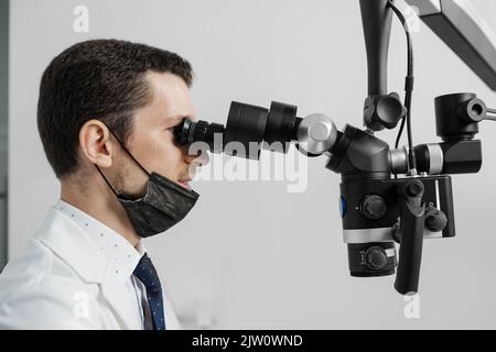 Male dentist using dental microscope treating female patient teeth at dental clinic office. Medicine, dentistry and health care concept. Dental equipm Stock Photo