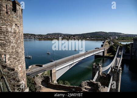 A view from Conwy Castle turrets of Deganwy, the old Telford suspension bridge and new road bridge opened in 1958 over the river Conwy in North Wales Stock Photo