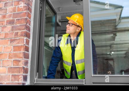 male builder in helmet looking out window Stock Photo