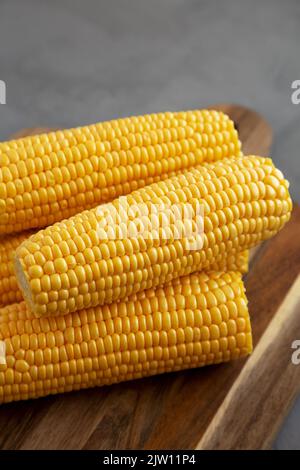 Fresh Raw Organic Yellow Sweet Corn on a wooden board on a gray surface, side view. Stock Photo