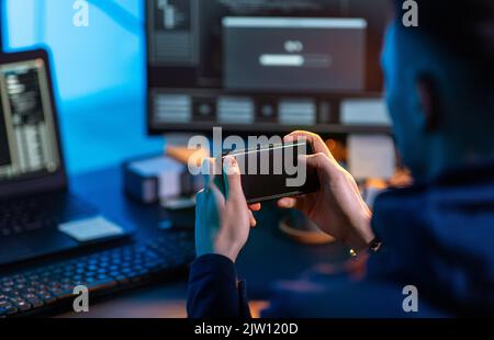 hacker with smartphone and computers in dark room Stock Photo