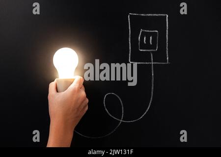 close up of hand holding lightbulb over chalkboard Stock Photo