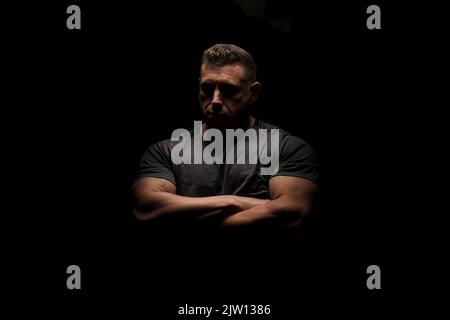 Big man with arms folded and looking into camera with top down lighting for a dramatic look. Stock Photo