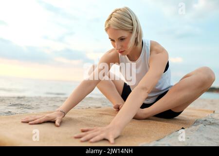 woman doing yoga stretching pose on beach Stock Photo