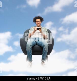 man with smartphone sitting in chair flying in sky Stock Photo
