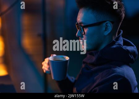 young man in glasses drinking coffee in dark room Stock Photo