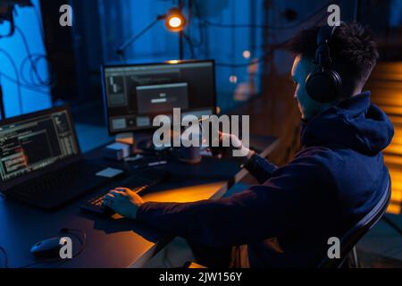 hacker with smartphone and computers in dark room Stock Photo