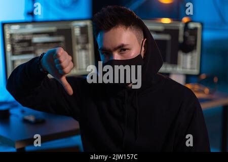 male hacker in mask showing thumbs down gesture Stock Photo