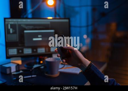 hacker with smartphone and computers in dark room Stock Photo