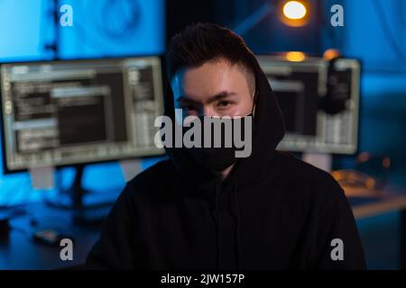 hacker wearing mask with computers in dark room Stock Photo