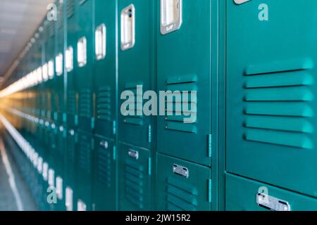 Green metal lockers along a nondescript hallway in a typical US High School.  No identifiable information included and nobody in the hall. Stock Photo
