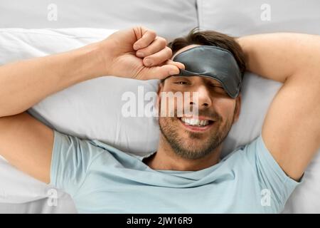 happy man in sleeping eye mask lying in bed Stock Photo