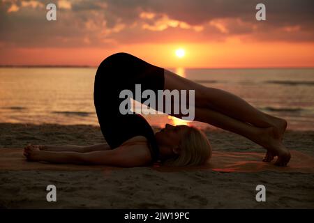 woman doing yoga plow pose on beach Stock Photo